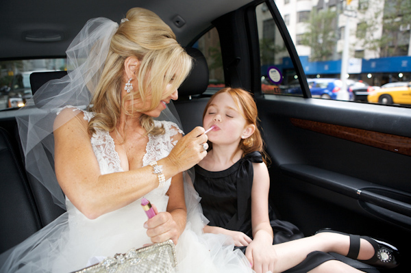 photo by New York based wedding photographer Merri Cry - bride putting lipgloss on the flower gild while sitting on the back of a car